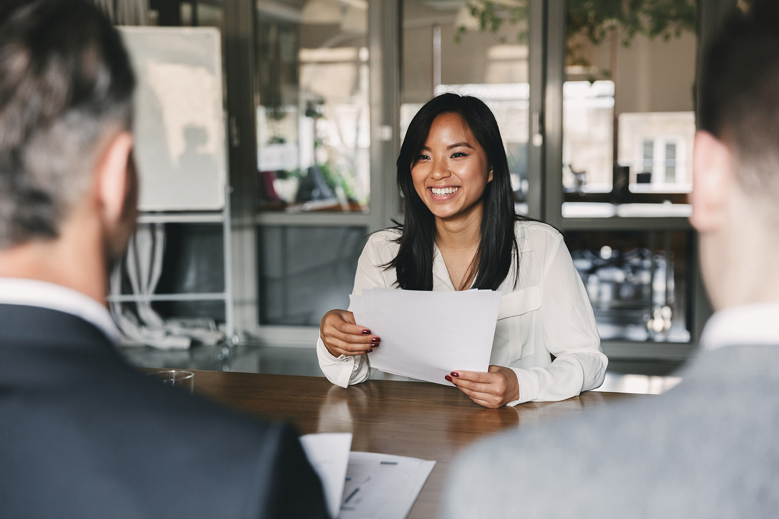 Woman smiling at a conference room table holding a piece of paper.